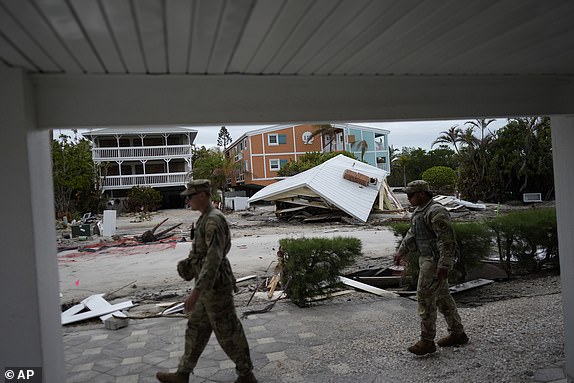 Members of the Florida Army National Guard walk past a destroyed home that was washed down the block by Hurricane Helene, as they check for any remaining residents ahead of the arrival of Hurricane Milton, Tuesday, Oct. 8, 2024, on Anna Maria Island, Fla. (AP Photo/Rebecca Blackwell)