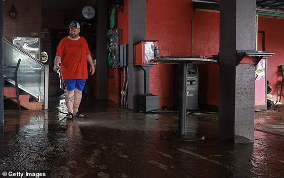 PUNTA GORDA - OCTOBER 10: Matt Schafer uses a water hose to clean the mud off of the floor at the Celtic Ray Public House restaurant/bar after it was inundated with flood waters when Hurricane Milton passed through the area on October 10, 2024, in Punta Gorda, Florida. The storm made landfall as a Category 3 hurricane in the Siesta Key area of Florida, causing damage and flooding throughout Central Florida. (Photo by Joe Raedle/Getty Images)